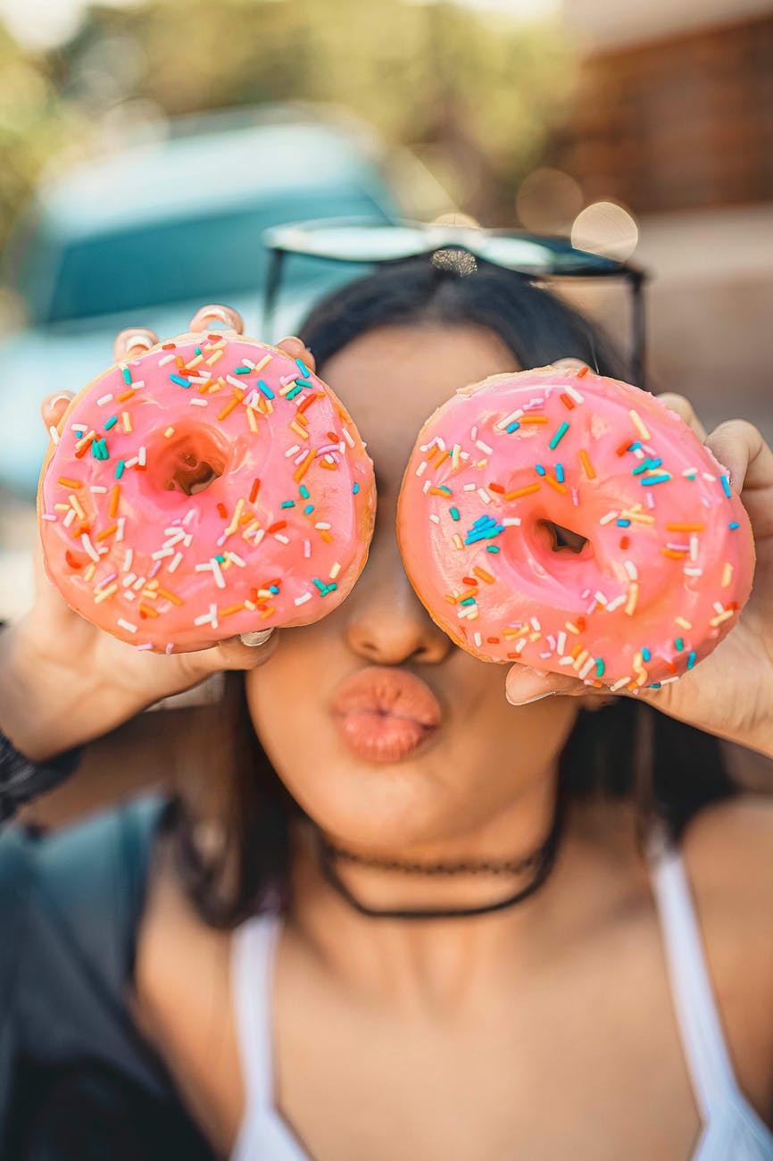 woman wearing white tank top holding two donuts